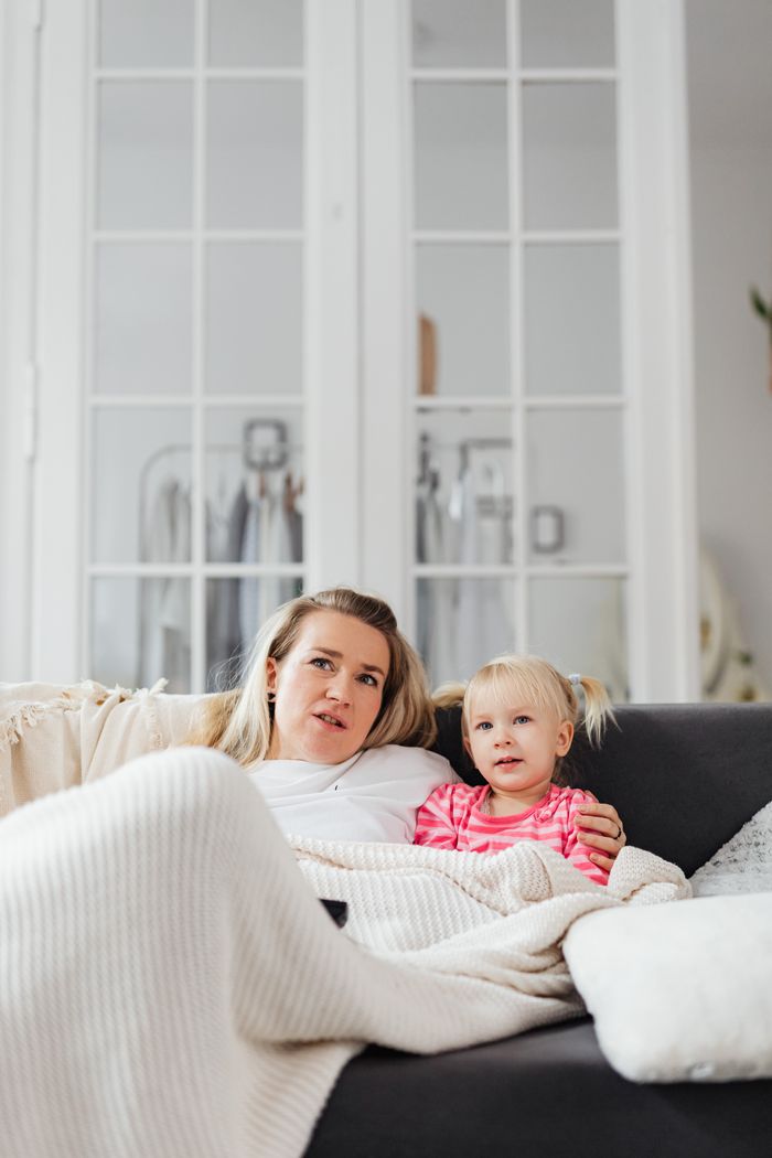 Mother and daughter bonding on a cozy couch, wrapped in a blanket indoors.